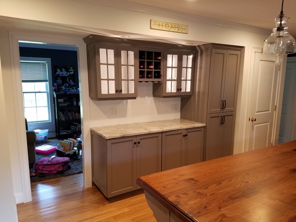 This is an example of a mid-sized transitional galley eat-in kitchen in Other with a farmhouse sink, recessed-panel cabinets, grey cabinets, wood benchtops, white splashback, subway tile splashback, stainless steel appliances, light hardwood floors, with island and brown floor.