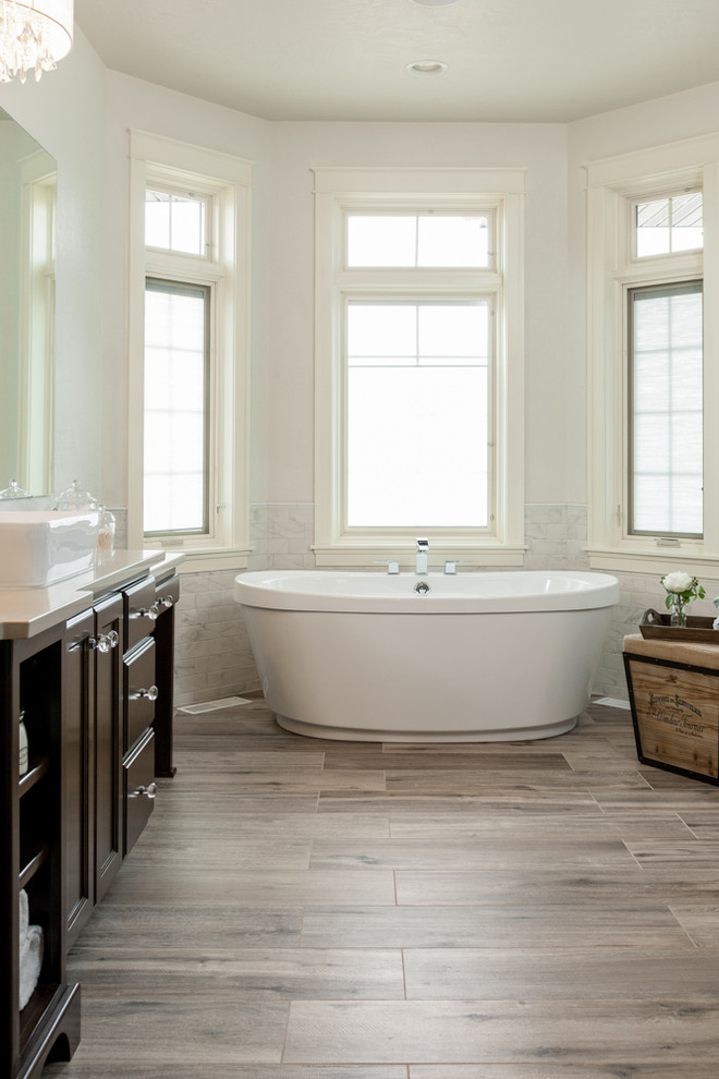 This is an example of a large traditional master bathroom in Other with recessed-panel cabinets, dark wood cabinets, a freestanding tub, brown tile, porcelain tile, white walls, porcelain floors, a vessel sink, quartzite benchtops and brown floor.