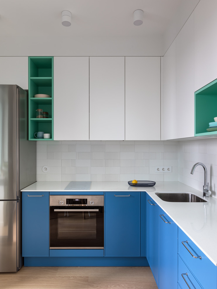 Moderne Küche ohne Insel in L-Form mit Unterbauwaschbecken, flächenbündigen Schrankfronten, blauen Schränken, Küchenrückwand in Weiß, Küchengeräten aus Edelstahl, hellem Holzboden, beigem Boden und weißer Arbeitsplatte in Sonstige
