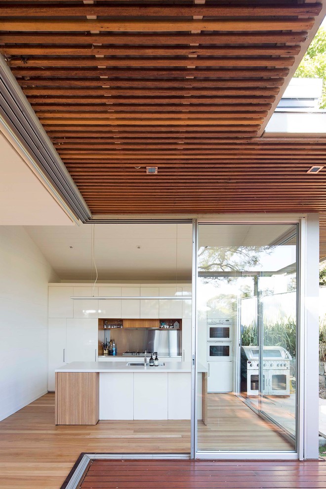 Inspiration for a mid-sized beach style galley eat-in kitchen in Sydney with an undermount sink, flat-panel cabinets, white cabinets, quartz benchtops, metallic splashback, stainless steel appliances, light hardwood floors and with island.