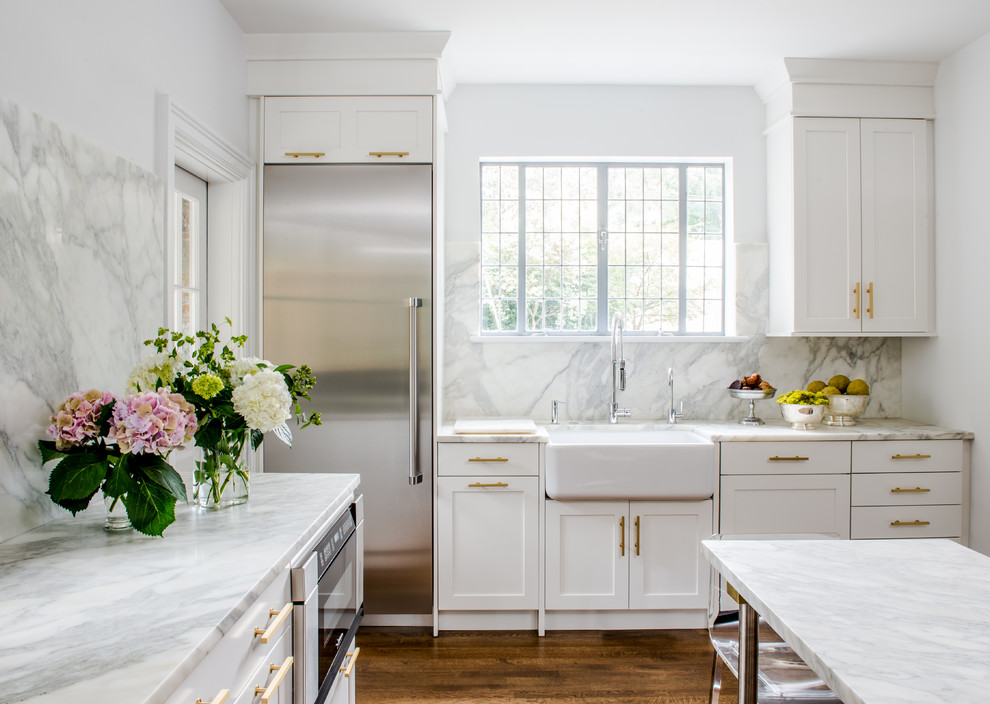 Design ideas for a large transitional l-shaped separate kitchen in DC Metro with a farmhouse sink, recessed-panel cabinets, white cabinets, marble benchtops, white splashback, marble splashback, stainless steel appliances, medium hardwood floors, with island and brown floor.
