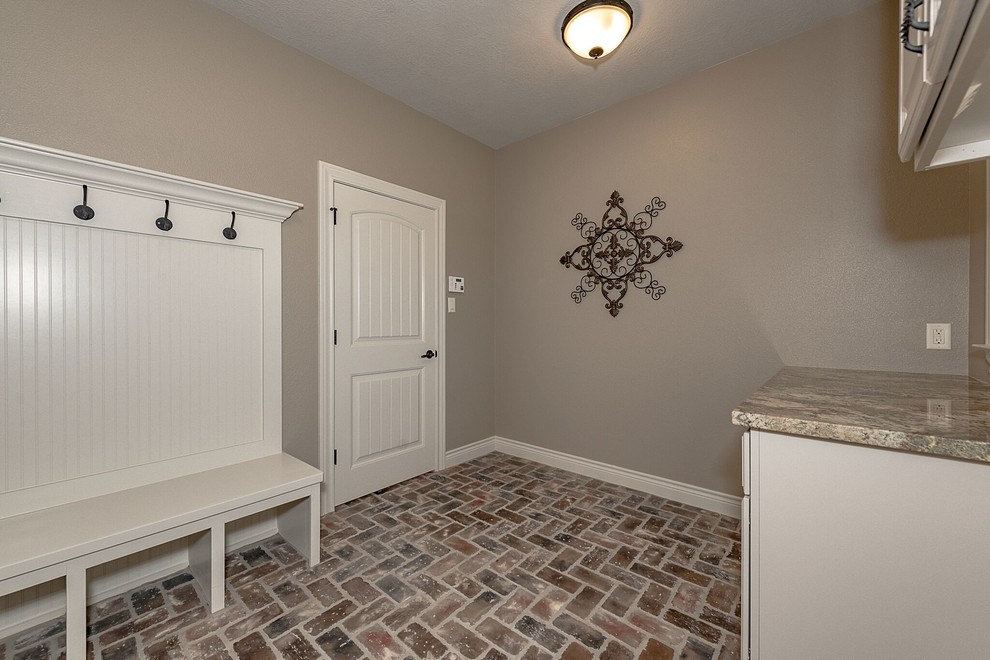 This is an example of a mid-sized country single-wall utility room in Austin with shaker cabinets, white cabinets, granite benchtops, beige walls, brick floors and brown floor.