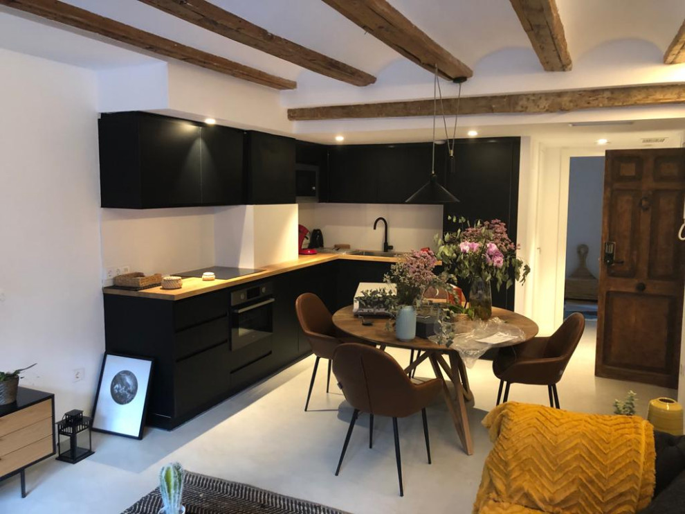 Small contemporary l-shaped eat-in kitchen in Valencia with flat-panel cabinets, black cabinets, wood benchtops, black appliances, concrete floors, no island, grey floor and exposed beam.