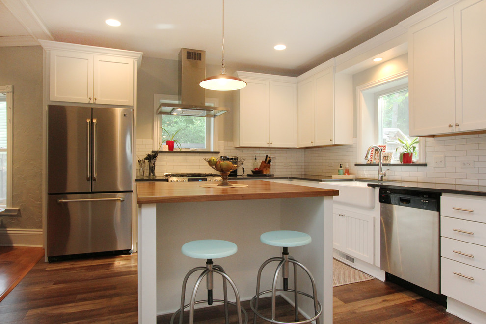 Photo of a small country l-shaped eat-in kitchen in Grand Rapids with a farmhouse sink, shaker cabinets, white cabinets, quartz benchtops, white splashback, subway tile splashback, stainless steel appliances, medium hardwood floors and with island.