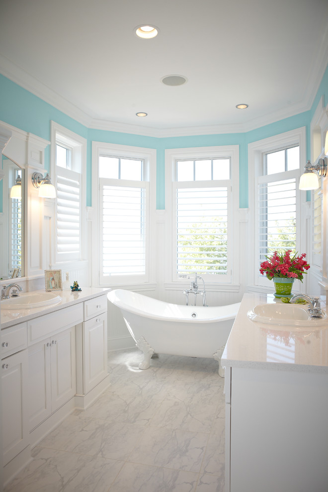 This is an example of a large traditional master bathroom in Grand Rapids with a drop-in sink, raised-panel cabinets, white cabinets, a claw-foot tub, quartzite benchtops, a two-piece toilet, blue walls, marble floors and white floor.