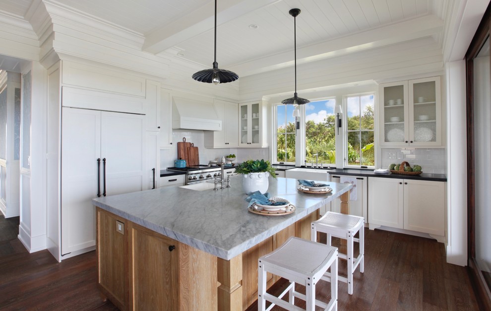 Inspiration for a tropical l-shaped kitchen in Hawaii with a farmhouse sink, shaker cabinets, white cabinets, white splashback, panelled appliances, medium hardwood floors, with island, brown floor and grey benchtop.