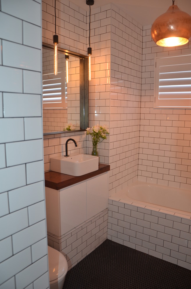 Photo of a contemporary bathroom in Sydney with a vessel sink, an alcove tub, a shower/bathtub combo, a one-piece toilet, flat-panel cabinets, white cabinets, wood benchtops, white tile and ceramic tile.