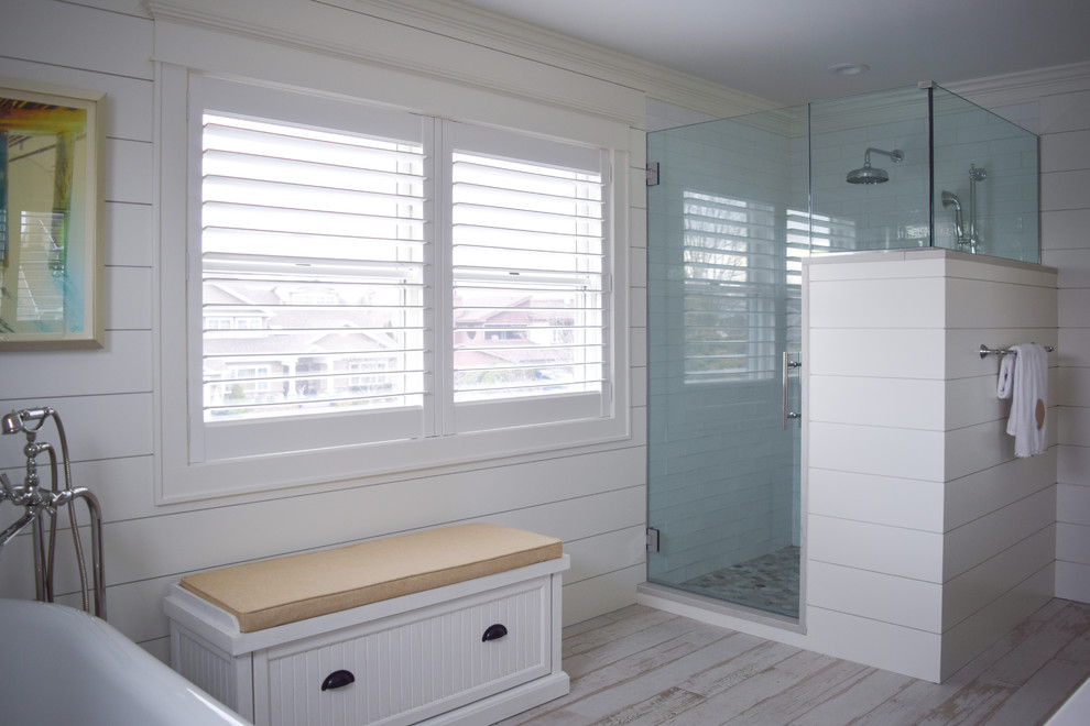 Large beach style master bathroom in New York with flat-panel cabinets, distressed cabinets, a freestanding tub, a double shower, a one-piece toilet, white walls, light hardwood floors, an undermount sink, engineered quartz benchtops, a hinged shower door and white benchtops.