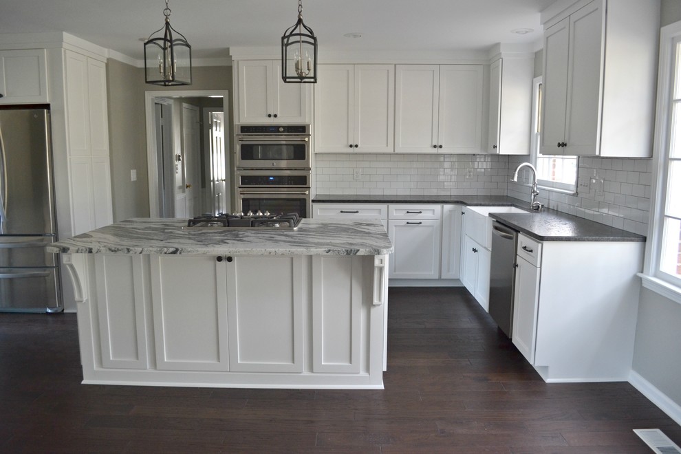 Inspiration for a large transitional l-shaped dark wood floor open concept kitchen remodel with a farmhouse sink, shaker cabinets, white cabinets, marble countertops, white backsplash, subway tile backsplash, stainless steel appliances and an island