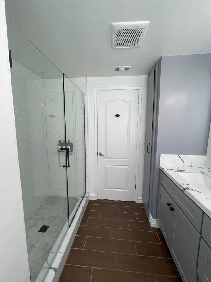 Пример оригинального дизайна: узкая и длинная детская ванная комната среднего размера в стиле кантри с фасадами в стиле шейкер, серыми фасадами, душем в нише, унитазом-моноблоком, белой плиткой, керамогранитной плиткой, белыми стенами, полом из керамогранита, врезной раковиной, столешницей из искусственного кварца, коричневым полом, душем с распашными дверями, черной столешницей, тумбой под две раковины и встроенной тумбой