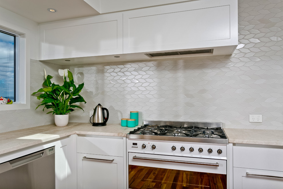 Design ideas for a small contemporary u-shaped eat-in kitchen in Auckland with an undermount sink, white cabinets, granite benchtops, white splashback, mosaic tile splashback, white appliances, medium hardwood floors and no island.