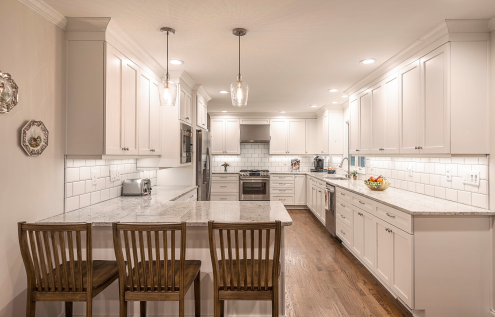 Mid-sized l-shaped eat-in kitchen in Atlanta with a drop-in sink, recessed-panel cabinets, white cabinets, granite benchtops, white splashback, subway tile splashback, stainless steel appliances, medium hardwood floors, a peninsula, brown floor and yellow benchtop.