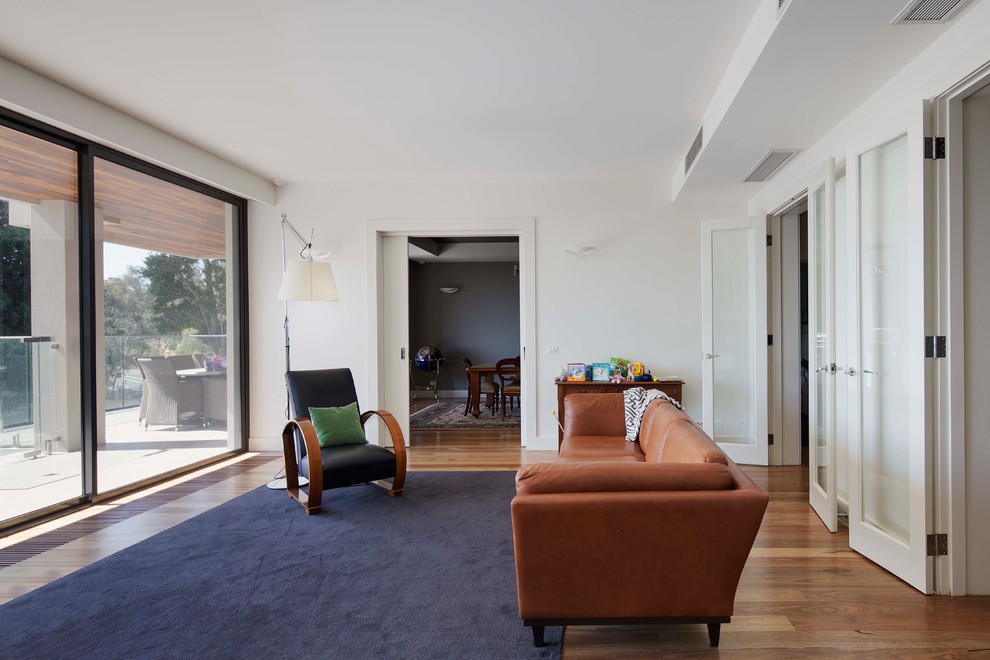 Large midcentury enclosed living room in Melbourne with white walls, light hardwood floors and no fireplace.