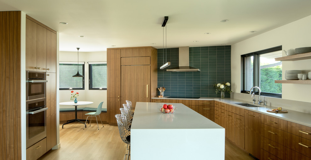 This is an example of a mid-sized midcentury u-shaped kitchen in Portland with flat-panel cabinets, medium wood cabinets, grey splashback, stainless steel appliances, light hardwood floors, with island, brown floor and grey benchtop.