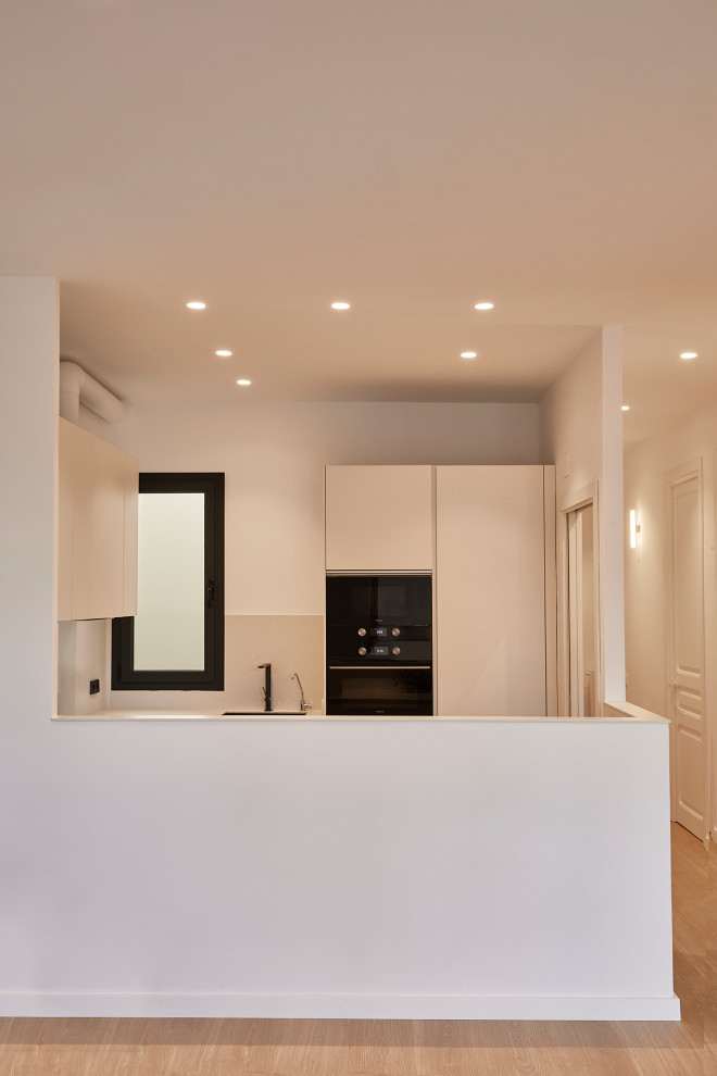 Imagen de cocina abovedada nórdica grande abierta con fregadero encastrado, puertas de armario beige, encimera de terrazo, salpicadero beige, puertas de cuarzo sintético, electrodomésticos negros, suelo de madera clara, península, suelo marrón y encimeras beige