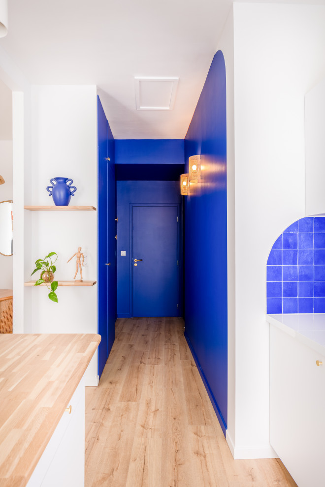 Maritim inredning av en liten hall, med blå väggar, ljust trägolv, en enkeldörr och en blå dörr