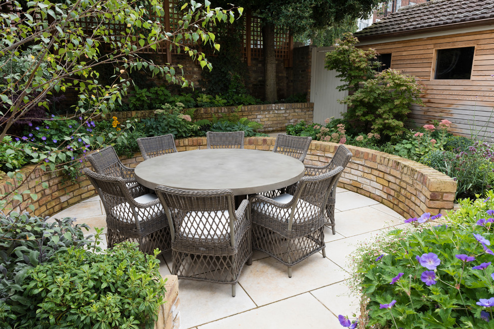 Design ideas for a mid-sized transitional backyard patio in London with natural stone pavers and no cover.
