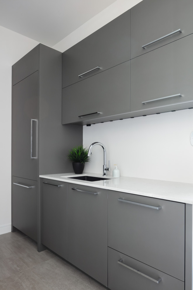 Inspiration for a small contemporary single-wall separate kitchen in Tampa with an undermount sink, flat-panel cabinets, grey cabinets, quartz benchtops, grey splashback, engineered quartz splashback, panelled appliances, porcelain floors, no island, grey floor and grey benchtop.