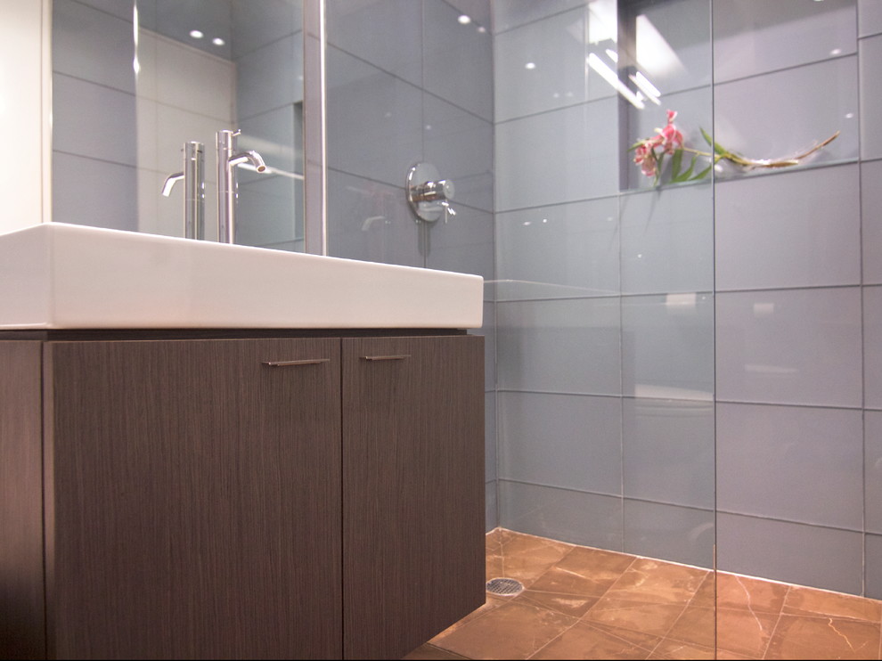 This is an example of a small modern 3/4 bathroom with flat-panel cabinets, brown cabinets, a curbless shower, blue tile, glass tile, limestone floors, engineered quartz benchtops, brown floor, an open shower and white benchtops.
