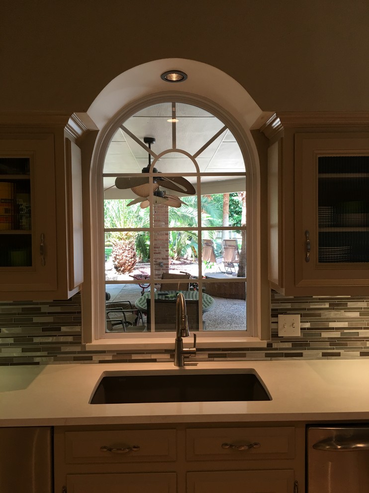 Inspiration for a mid-sized transitional u-shaped kitchen remodel in Houston with an undermount sink, recessed-panel cabinets, beige cabinets, solid surface countertops, multicolored backsplash, glass tile backsplash, stainless steel appliances and a peninsula