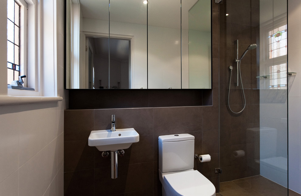 Photo of a small contemporary master bathroom in Adelaide with a wall-mount sink, glass-front cabinets, an open shower, a one-piece toilet, brown tile, porcelain tile, white walls and porcelain floors.