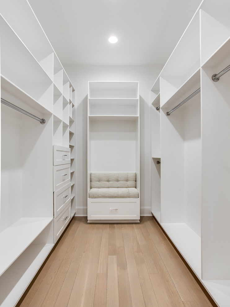 Example of a large transitional gender-neutral light wood floor walk-in closet design with recessed-panel cabinets and white cabinets