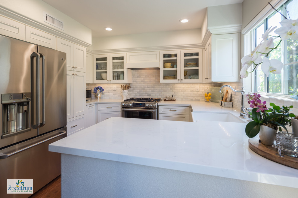 This is an example of a small arts and crafts u-shaped eat-in kitchen in San Diego with a farmhouse sink, beaded inset cabinets, white cabinets, quartz benchtops, white splashback, subway tile splashback, stainless steel appliances, dark hardwood floors and a peninsula.
