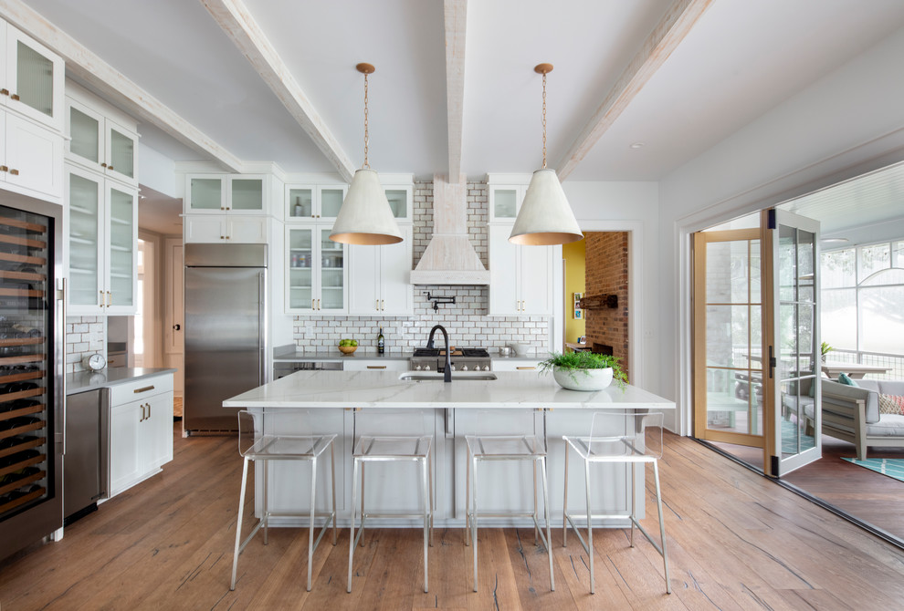 Design ideas for a beach style l-shaped kitchen in New Orleans with an undermount sink, recessed-panel cabinets, white cabinets, white splashback, subway tile splashback, stainless steel appliances, medium hardwood floors, with island, brown floor and white benchtop.