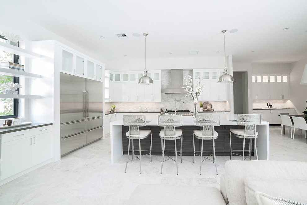 Inspiration for an expansive contemporary l-shaped open plan kitchen in Miami with an undermount sink, shaker cabinets, white cabinets, quartzite benchtops, beige splashback, stone tile splashback, stainless steel appliances, porcelain floors, with island, white floor and black benchtop.