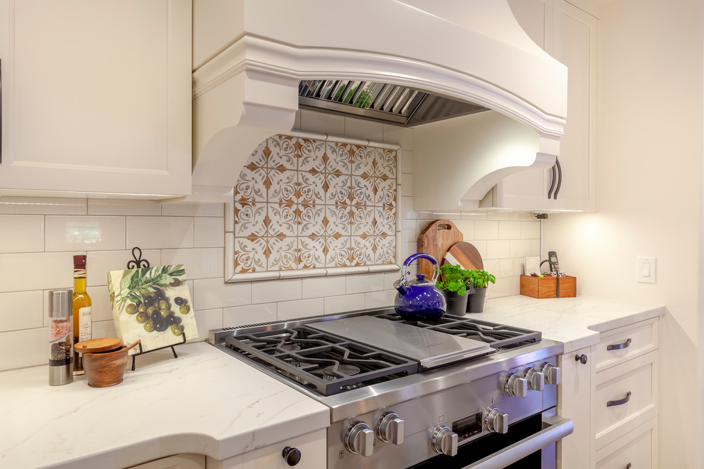 Photo of a mid-sized mediterranean eat-in kitchen in Los Angeles with an undermount sink, recessed-panel cabinets, white cabinets, quartz benchtops, white splashback, porcelain splashback, stainless steel appliances, cement tiles, with island, red floor and white benchtop.