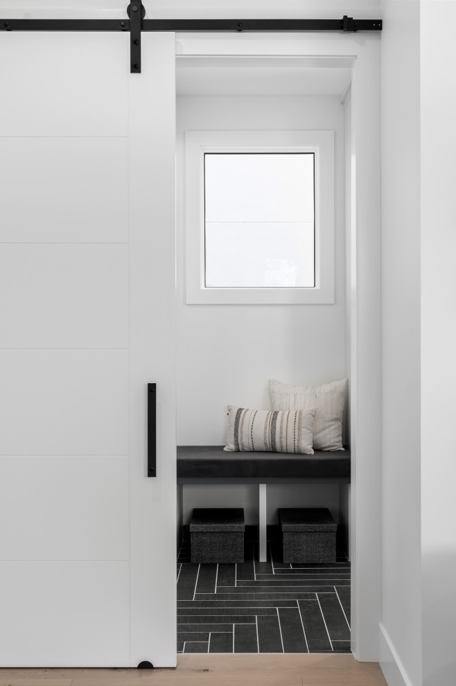 Modern inredning av ett mellanstort kapprum, med svarta väggar, klinkergolv i porslin, en skjutdörr, en vit dörr och svart golv