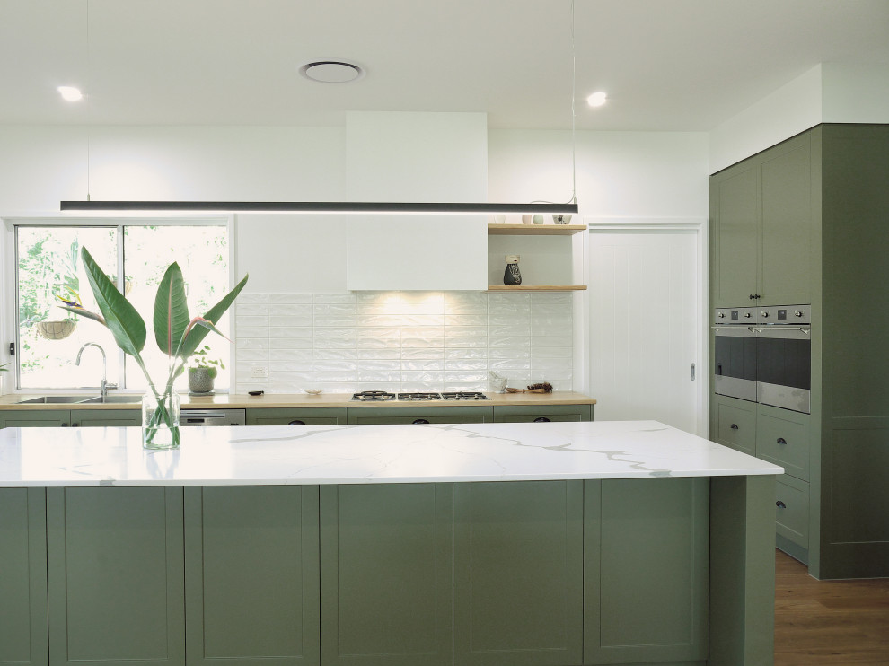 Inspiration for a mid-sized contemporary galley eat-in kitchen in Sunshine Coast with a double-bowl sink, recessed-panel cabinets, green cabinets, quartz benchtops, white splashback, ceramic splashback, stainless steel appliances, vinyl floors, with island, brown floor and white benchtop.
