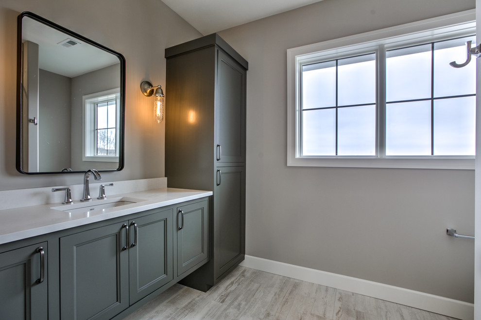 Inspiration for a mid-sized country bathroom in Omaha with recessed-panel cabinets, grey cabinets, grey walls, light hardwood floors, an undermount sink, engineered quartz benchtops, grey floor and white benchtops.