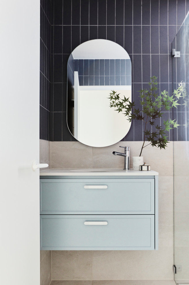 Mid-sized beach style multicolored tile and mosaic tile porcelain tile, gray floor and single-sink corner shower photo in Sydney with furniture-like cabinets, blue cabinets, a one-piece toilet, gray walls, solid surface countertops, white countertops and a floating vanity