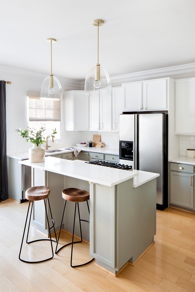 Inspiration for a mid-sized transitional l-shaped kitchen in Baltimore with white cabinets, white splashback, subway tile splashback, stainless steel appliances, light hardwood floors, with island, white benchtop, an undermount sink, shaker cabinets and beige floor.