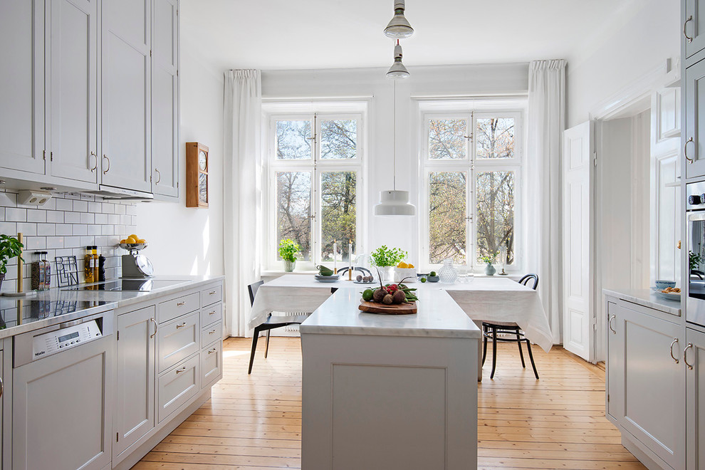 Photo of a mid-sized transitional galley eat-in kitchen in Stockholm with recessed-panel cabinets, grey cabinets, white splashback, subway tile splashback, stainless steel appliances, medium hardwood floors, with island and marble benchtops.