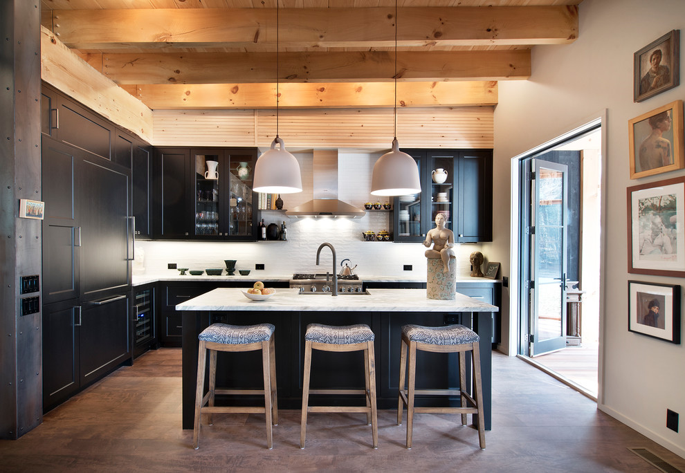 This is an example of a transitional l-shaped kitchen in New York with shaker cabinets, black cabinets, white splashback, stainless steel appliances, medium hardwood floors, with island, brown floor and white benchtop.