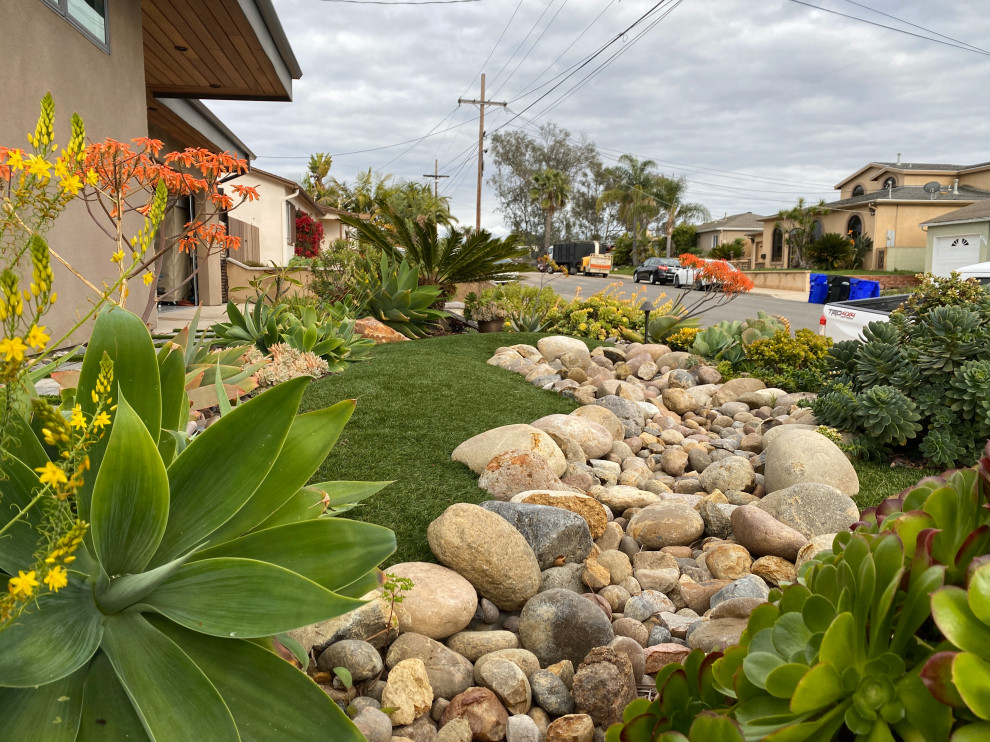 Photo of a mid-sized contemporary front yard full sun xeriscape for summer in San Diego with with lawn edging, river rock and a wood fence.