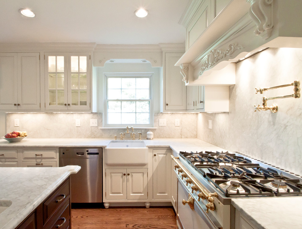 Photo of a traditional kitchen in DC Metro with beaded inset cabinets, a farmhouse sink, white splashback, stone slab splashback, stainless steel appliances, white cabinets and marble benchtops.