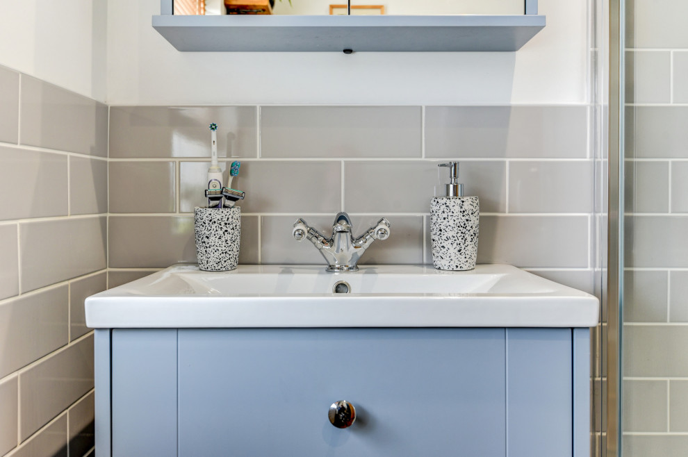 Klassisk inredning av ett litet badrum med dusch, med skåp i shakerstil, blå skåp, en hörndusch, en toalettstol med separat cisternkåpa, beige kakel, keramikplattor, vita väggar, ett nedsänkt handfat, brunt golv och dusch med skjutdörr