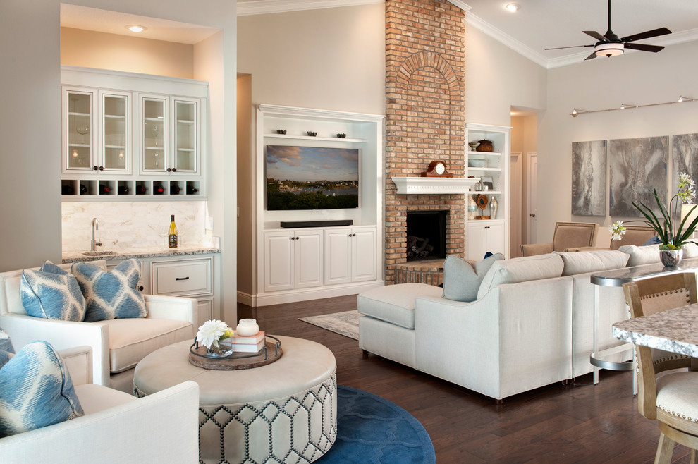 This is an example of a mediterranean open concept family room in Orlando with a home bar, beige walls, dark hardwood floors, a standard fireplace, a brick fireplace surround, a built-in media wall and brown floor.