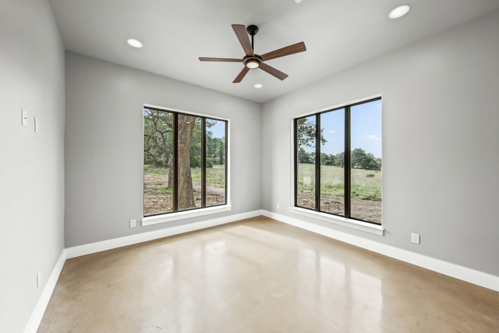 Inspiration for a mid-sized cottage freestanding desk concrete floor and brown floor study room remodel in Other with gray walls, a standard fireplace and a stacked stone fireplace