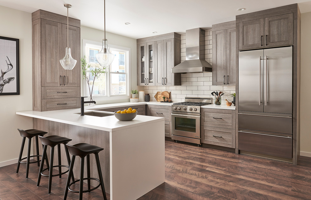 This is an example of a transitional u-shaped kitchen in Charleston with an undermount sink, shaker cabinets, brown cabinets, white splashback, stainless steel appliances, dark hardwood floors, a peninsula, brown floor and white benchtop.