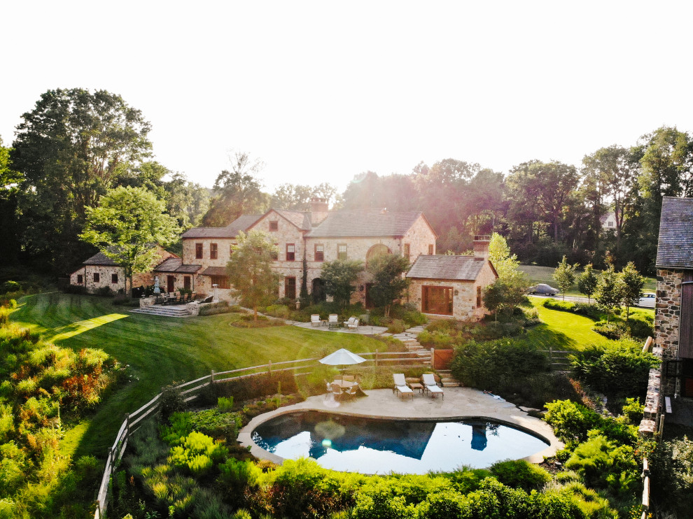 This is an example of a mid-sized country backyard kidney-shaped natural pool in Philadelphia with a pool house and natural stone pavers.