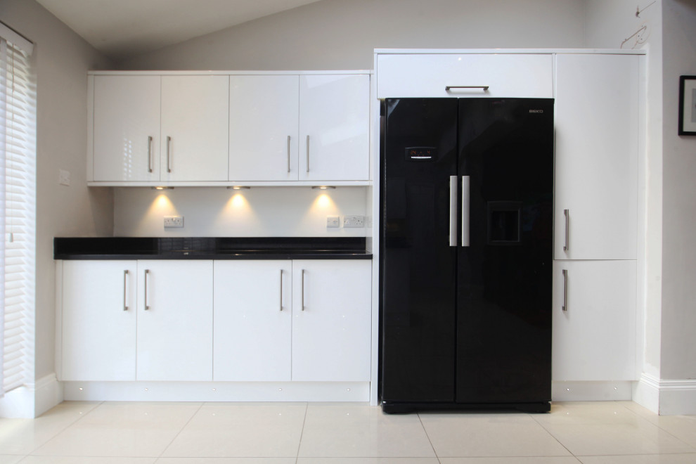Medium sized modern l-shaped open plan kitchen in Cheshire with a double-bowl sink, flat-panel cabinets, white cabinets, granite worktops, metallic splashback, metal splashback, black appliances, porcelain flooring, a breakfast bar, beige floors and black worktops.