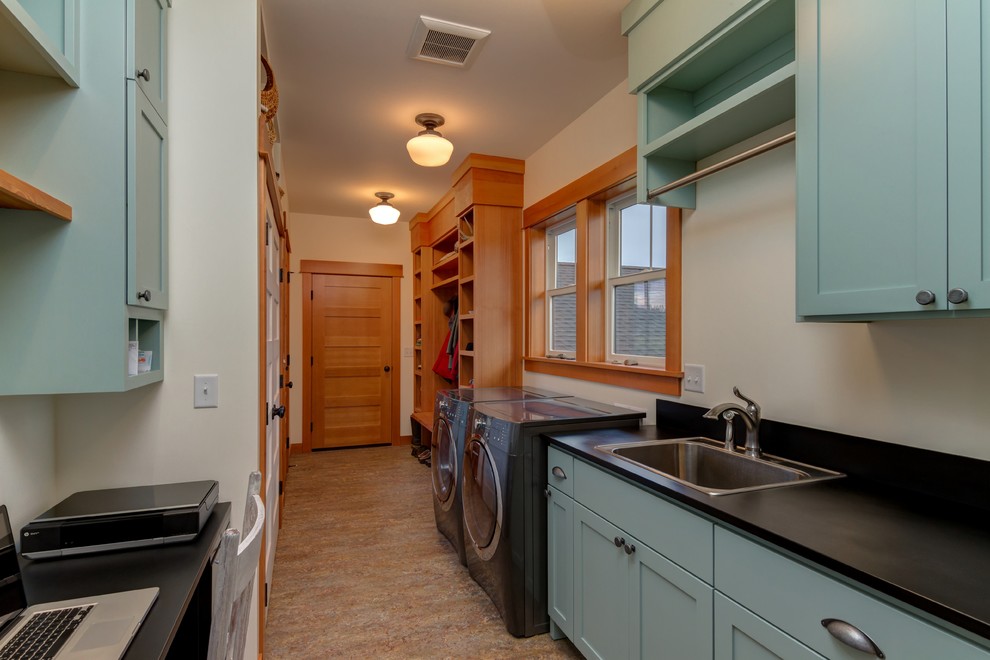 Photo of a large country l-shaped laundry room in Seattle with a farmhouse sink, raised-panel cabinets, white cabinets, wood benchtops, medium hardwood floors and black benchtop.