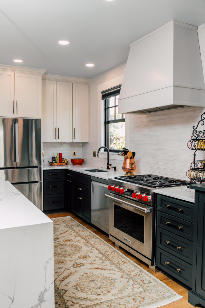 This is an example of a mid-sized transitional l-shaped open plan kitchen in Seattle with an undermount sink, shaker cabinets, green cabinets, quartz benchtops, white splashback, cement tile splashback, stainless steel appliances, light hardwood floors, with island, brown floor and white benchtop.