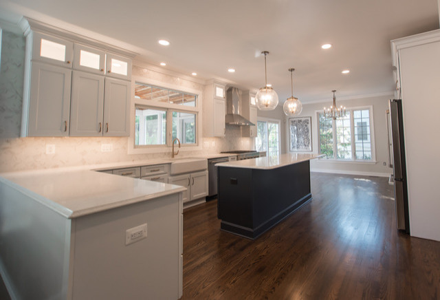 Example of a transitional medium tone wood floor and brown floor open concept kitchen design in Baltimore with a farmhouse sink, shaker cabinets, white cabinets, quartz countertops, white backsplash, porcelain backsplash, stainless steel appliances, an island and white countertops