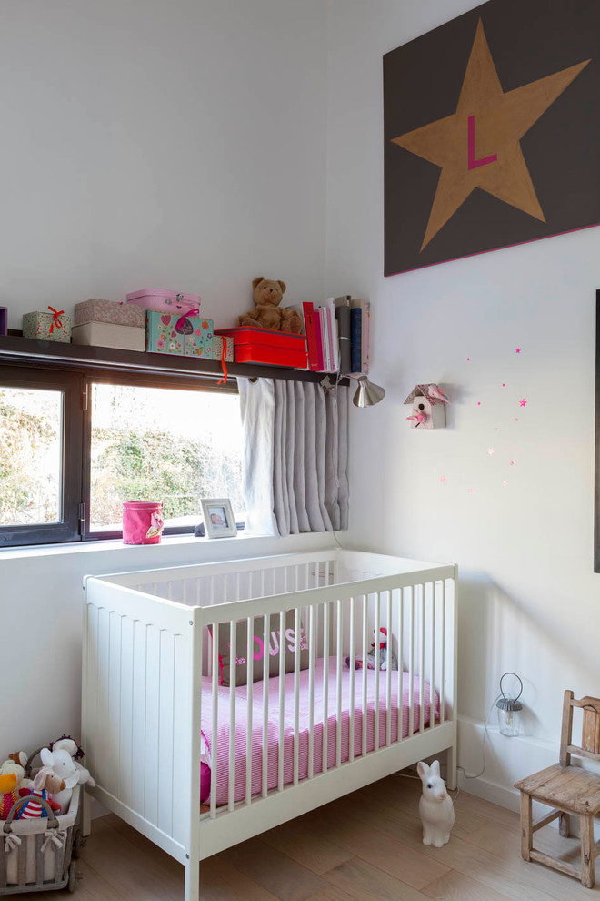 Design ideas for a mid-sized industrial nursery for girls in Paris with white walls, plywood floors and beige floor.