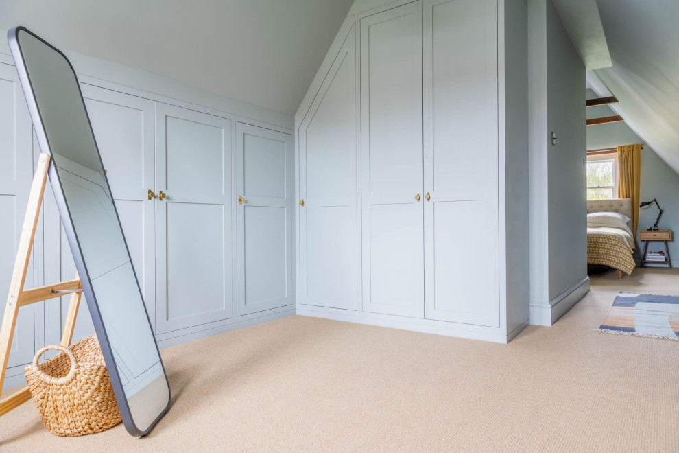 Mid-sized traditional gender-neutral walk-in wardrobe in Other with shaker cabinets, blue cabinets, carpet, beige floor and vaulted.